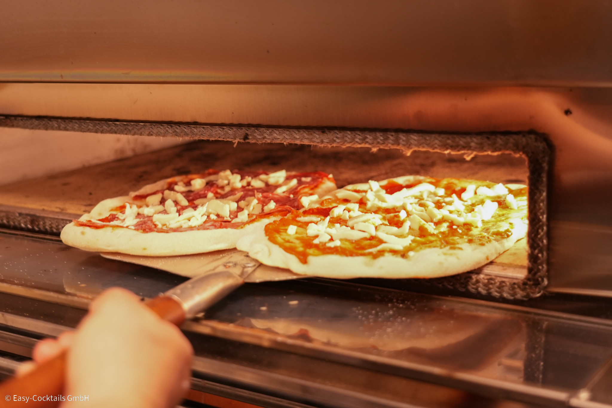 Pinsa Manufaktur Pinsa Ofen Zwei ungebackene, mit Tomatensoße und Käse belegte Pinsa Teiglinge, werden auf einem Schieber in den Ofen geschoben